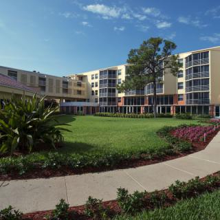 A college campus building surrounded by greenery and a clear blue sky.