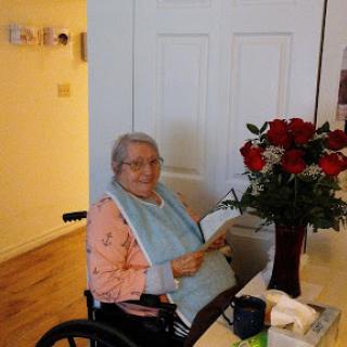 An elderly person enjoying a moment indoors, with a beautiful bouquet of red roses nearby.