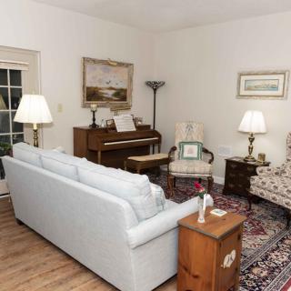 A cozy living room featuring a sofa, piano, and armchairs with warm lighting.