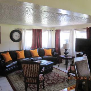 A cozy living room with a black leather sofa, orange pillows, a television, and an armchair.