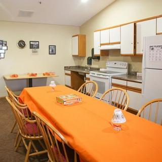 A cozy kitchen and dining area with an orange-tableclothed table and wooden chairs.
