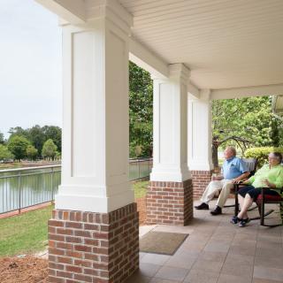 A couple relaxing on a porch overlooking a lake.