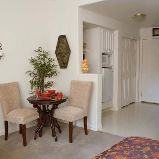 A cozy living space featuring a small dining area with two chairs, a round wooden table, and decorative elements including a plant and wall art.