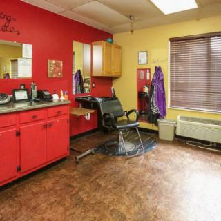 A cozy hair salon with vibrant red and yellow walls, featuring a styling chair, mirrors, and hairdressing equipment.