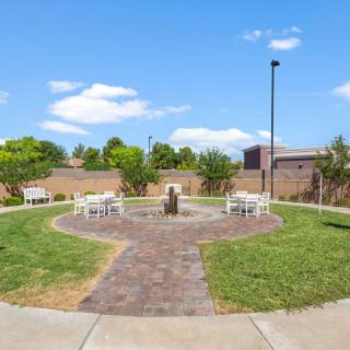 A serene garden with a central fountain, surrounded by benches and green grass under a clear blue sky.