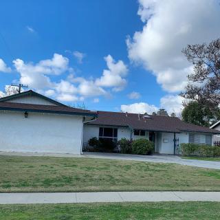 A suburban house with a front lawn and a driveway under a partly cloudy sky.