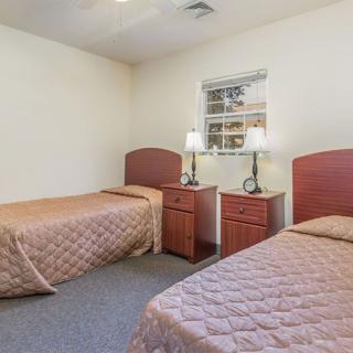 A simple bedroom featuring two twin beds with matching quilts, wooden headboards, and bedside tables with lamps.