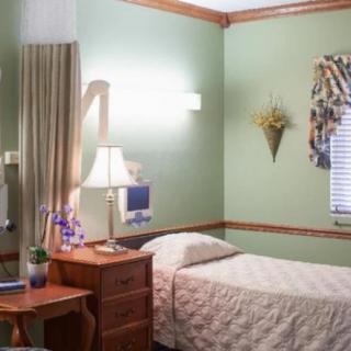A cozy bedroom with pastel green walls, featuring a single bed, a wooden nightstand with a lamp, and decorative curtains.