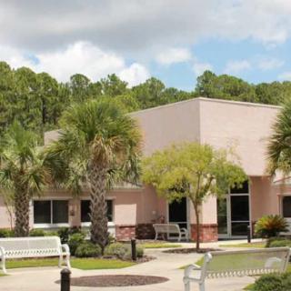 A building surrounded by palm trees and benches, set against a cloudy sky.
