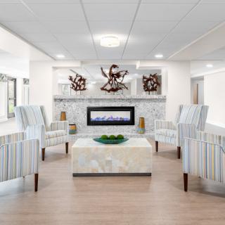 A modern living room with a central fireplace, surrounded by striped chairs and decorative wall art.