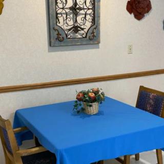 A dining area with a blue tablecloth, decorated with a floral centerpiece and wall art.