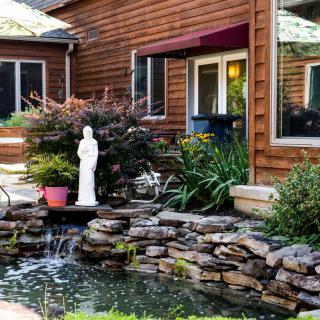 A serene garden scene with a pond and statue in front of a wooden house.