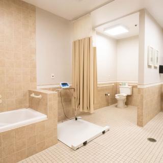 An accessible hospital bathroom with a bathtub, toilet, and privacy curtain.