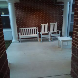 A porch with white wooden furniture against a brick wall.