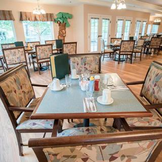 A cozy dining area with neatly set tables and comfortable chairs, featuring large windows and warm lighting.