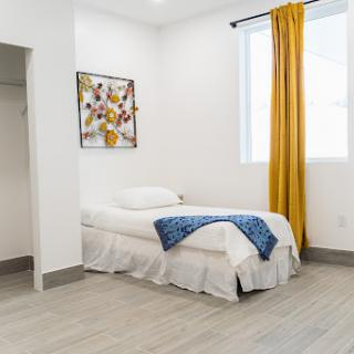 A minimalist bedroom featuring a single bed with white bedding, complemented by yellow curtains and a touch of artwork on the wall.