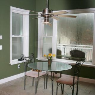 A cozy dining area with a glass table and chairs, set against green walls and large windows.