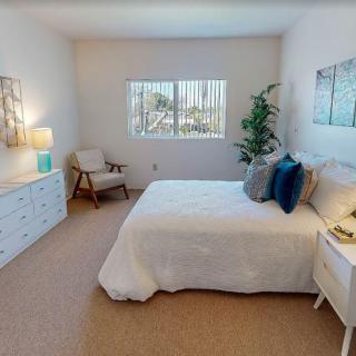 A cozy bedroom with modern decor, featuring a comfortable bed, dresser, and a window allowing natural light in.