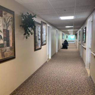 A long hallway in a nursing home with decorated walls and a person in a wheelchair at the end.