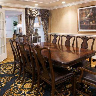 A traditional dining room with an elegant wooden table and chairs, complemented by a patterned carpet and wall art.