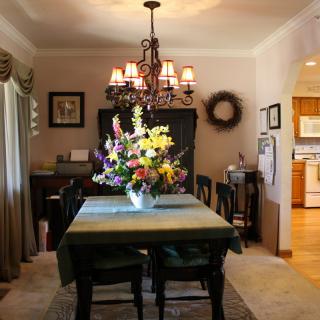 A cozy dining room with a chandelier and a flower arrangement centerpiece.