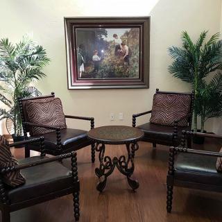 A cozy seating area with four chairs around a round table, adorned with plants and a framed painting on the wall.