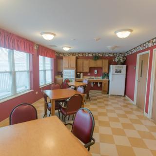 A kitchen and dining area with red walls, featuring multiple tables and chairs, a checkerboard floor, and several appliances.