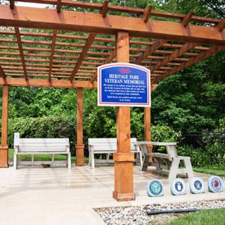 A memorial pergola with benches and military emblems placed in an outdoor garden setting.