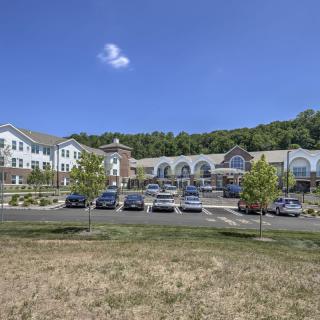A large building with a parking lot and cars, surrounded by trees under a clear blue sky.
