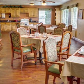 An inviting dining room with neatly arranged tables and chairs, featuring a view into a kitchen area.