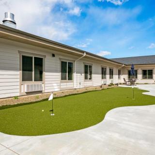 A sunny courtyard featuring a small putting green surrounded by a building.