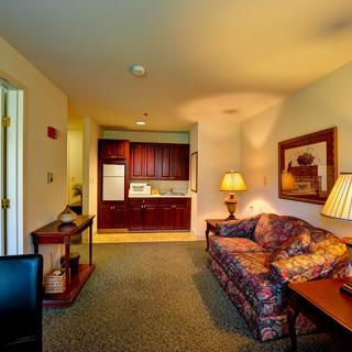 A cozy living room with a sofa, table lamps, and a view into a kitchenette with wooden cabinets.