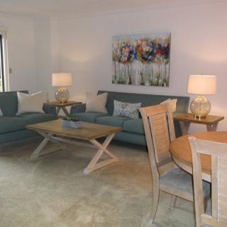 A cozy living room featuring two sofas, a coffee table, dining set, and decorative lamps with artwork on the wall.