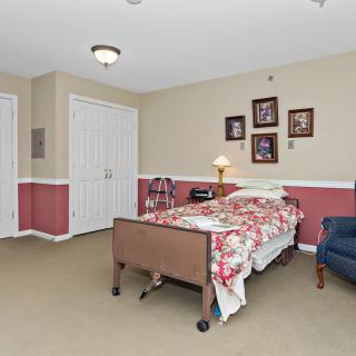 A well-furnished bedroom with a hospital bed, armchair, and decorative elements on the wall.