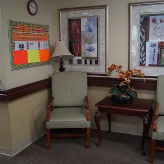 A cozy waiting room with chairs, a small table, and decorative paintings on the wall.