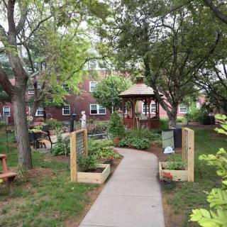 A peaceful garden with a pathway leading to a wooden gazebo surrounded by lush trees.