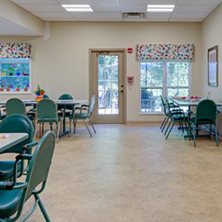 A bright and clean dining area with several tables and chairs, decorated with patterned curtains and ample natural light from large windows.