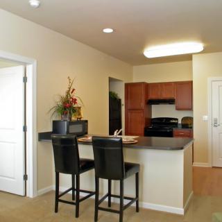 A modern apartment kitchen with a counter and two stools, featuring minimalist design elements.