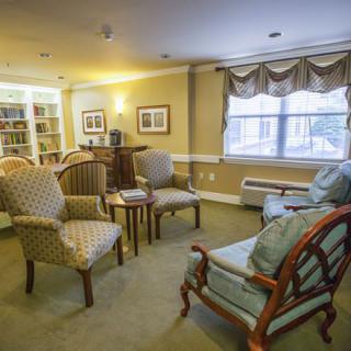 A cozy living room with several chairs, a small table, and bookshelves in the corner.
