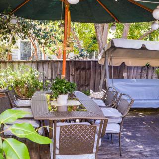 A cozy outdoor patio area with a table, chairs, and an umbrella surrounded by greenery.