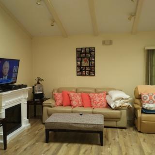 A cozy living room with a comfortable sofa, colorful cushions, a television above the fireplace, and a coffee table in front.