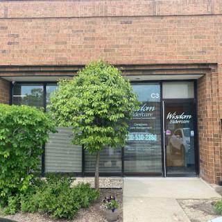 A storefront with large windows and a small tree in front, set against a brick wall.