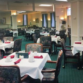 An empty restaurant dining room with neatly arranged tables covered in white tablecloths.