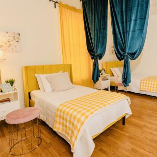 A cozy bedroom featuring twin beds with yellow accents and striking blue curtains, set against a warm wooden floor.