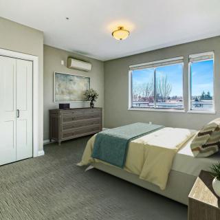 A modern and minimalist bedroom with a large window, carpeted floor, and stylish furniture.