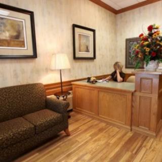 A cozy reception area featuring a wooden desk, comfortable sofa, framed artwork on the walls, and a lamp providing warm lighting.