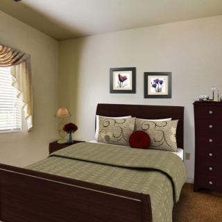 A cozy bedroom with a neatly made bed, decorated with floral pillows and artwork on the walls.