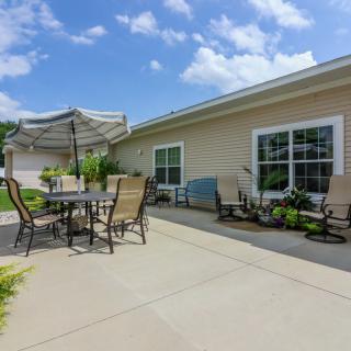 A sunny backyard patio with outdoor furniture and an umbrella, adjacent to a house.