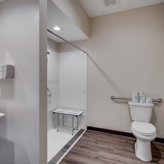 A modern, accessible bathroom featuring a walk-in shower with a bench and a toilet with grab bars.