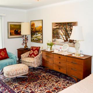 A cozy living room with vintage furnishings, including an armchair, a patterned rug, and decorated with paintings and lamps.